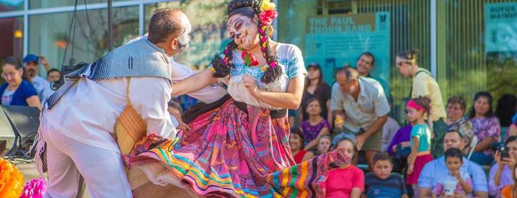 A man and woman in colorful, traditional Dia de los Muertos attire dance in front of a crowd at the annual event in Mesa, AZ.
